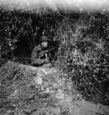 Grease gun toting GI soldier in a foxhole near the front lines during the Battle of the Bulge..jpg