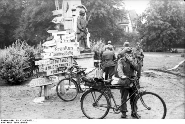 Bundesarchiv_Bild_101I-301-1951-11,_Nordfrankreich,_deutsche_Soldaten_an_Wegweiser.jpg